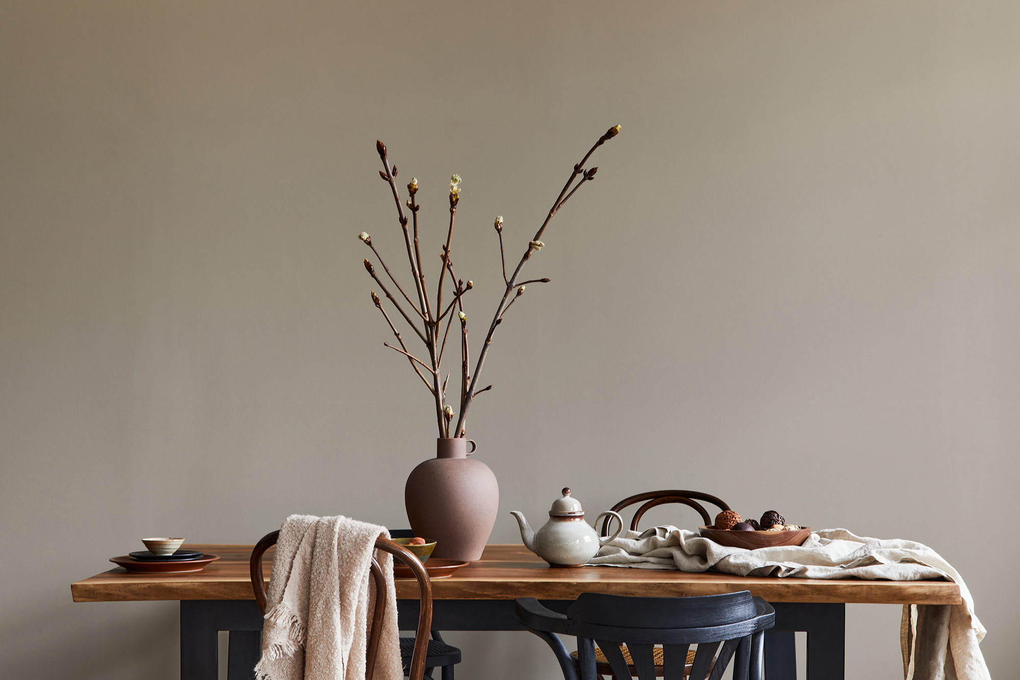 Stylish rustic interior of dining room with walnut wooden table, retro chairs, decoration, dried flower in vase in minimalist home decor. Template. Neutral background wall.